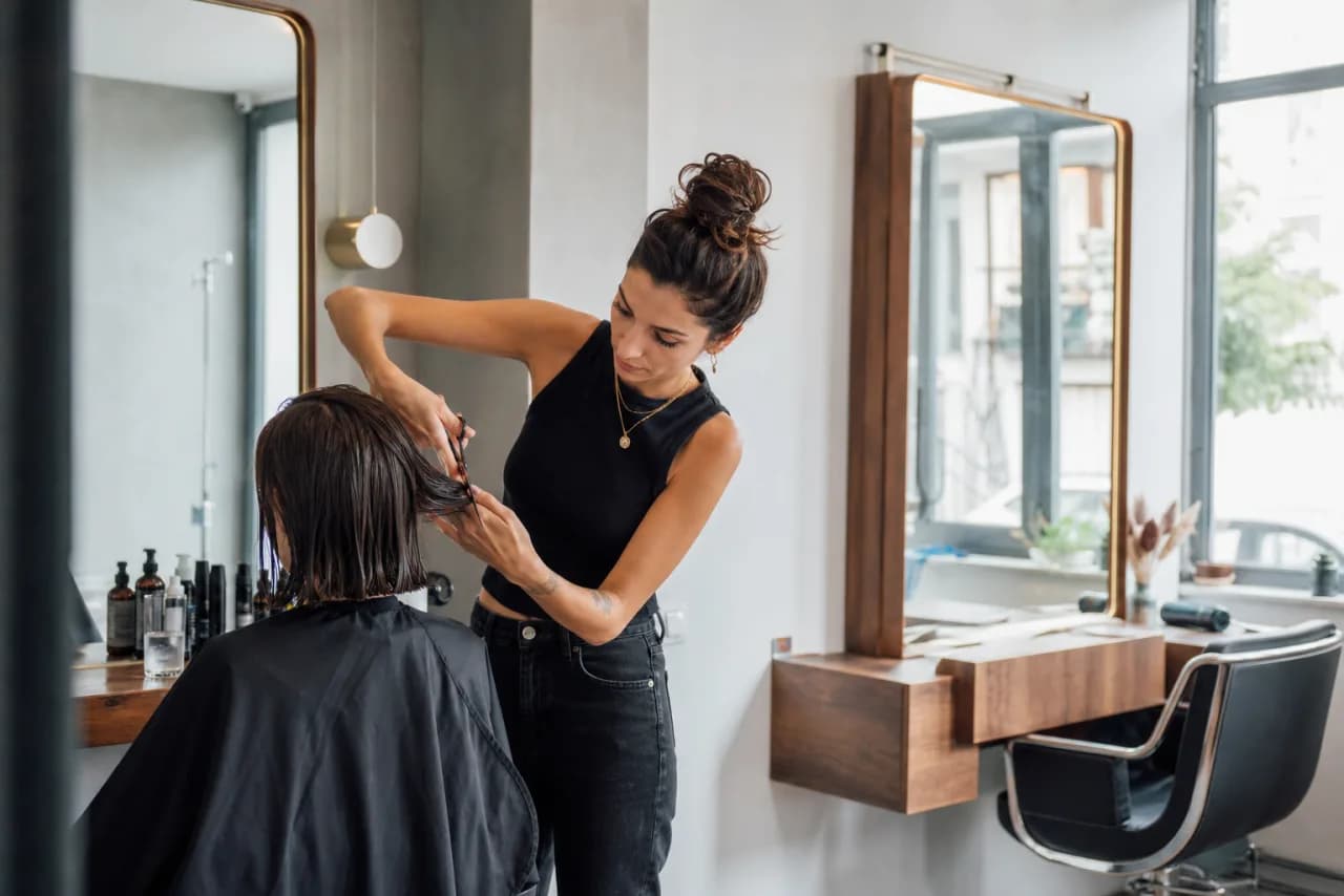 Aydınlık bir kuaför salonunda müşterinin saçını şekillendiren kuaför